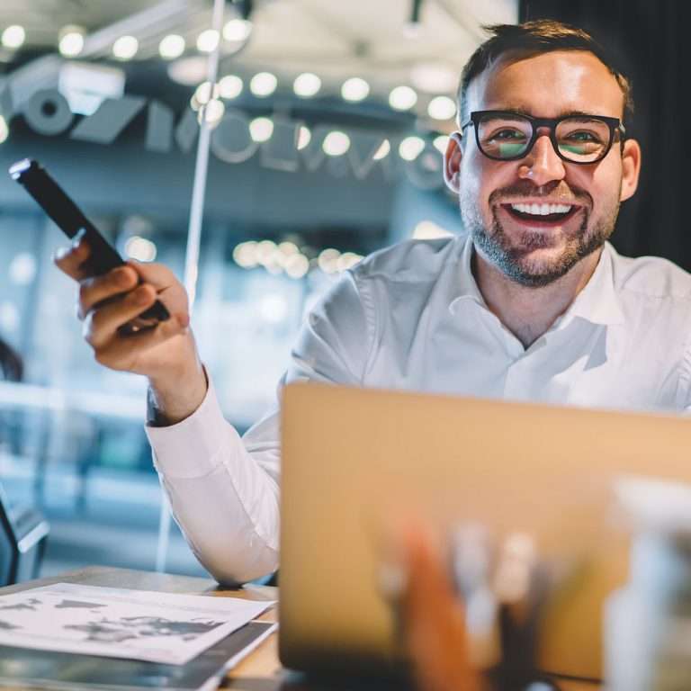 Porträt eines fröhlichen, aufgeregten Geschäftsmannes mit Brille, der während der Arbeitszeit in einem Unternehmen zufrieden in die Kamera lächelt.
